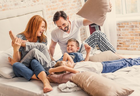 Mutter, Vater und Kinder sitzen auf dem Bett und lachen miteinander